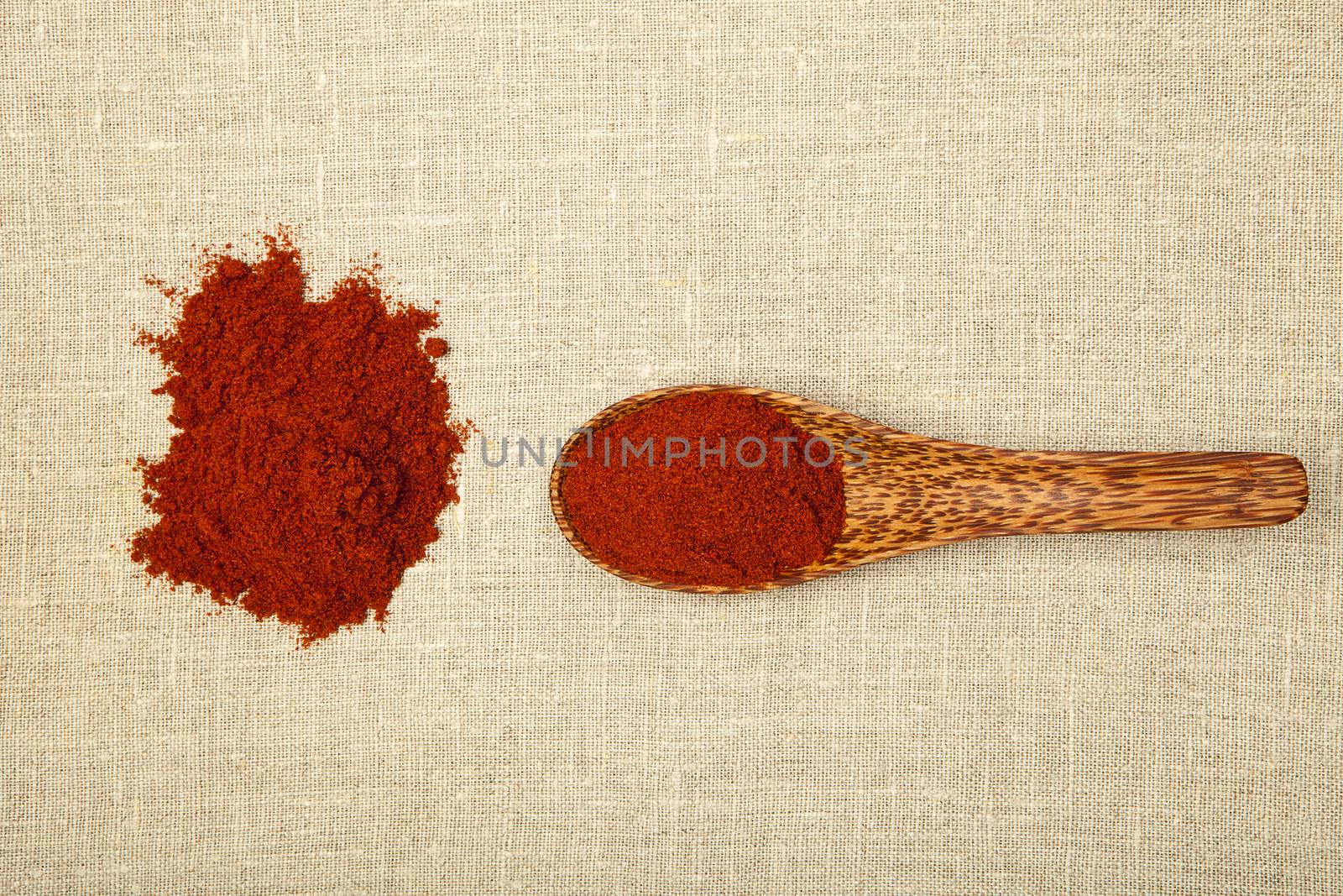 Red chilli spice on bamboo spoon on brown background, top view.