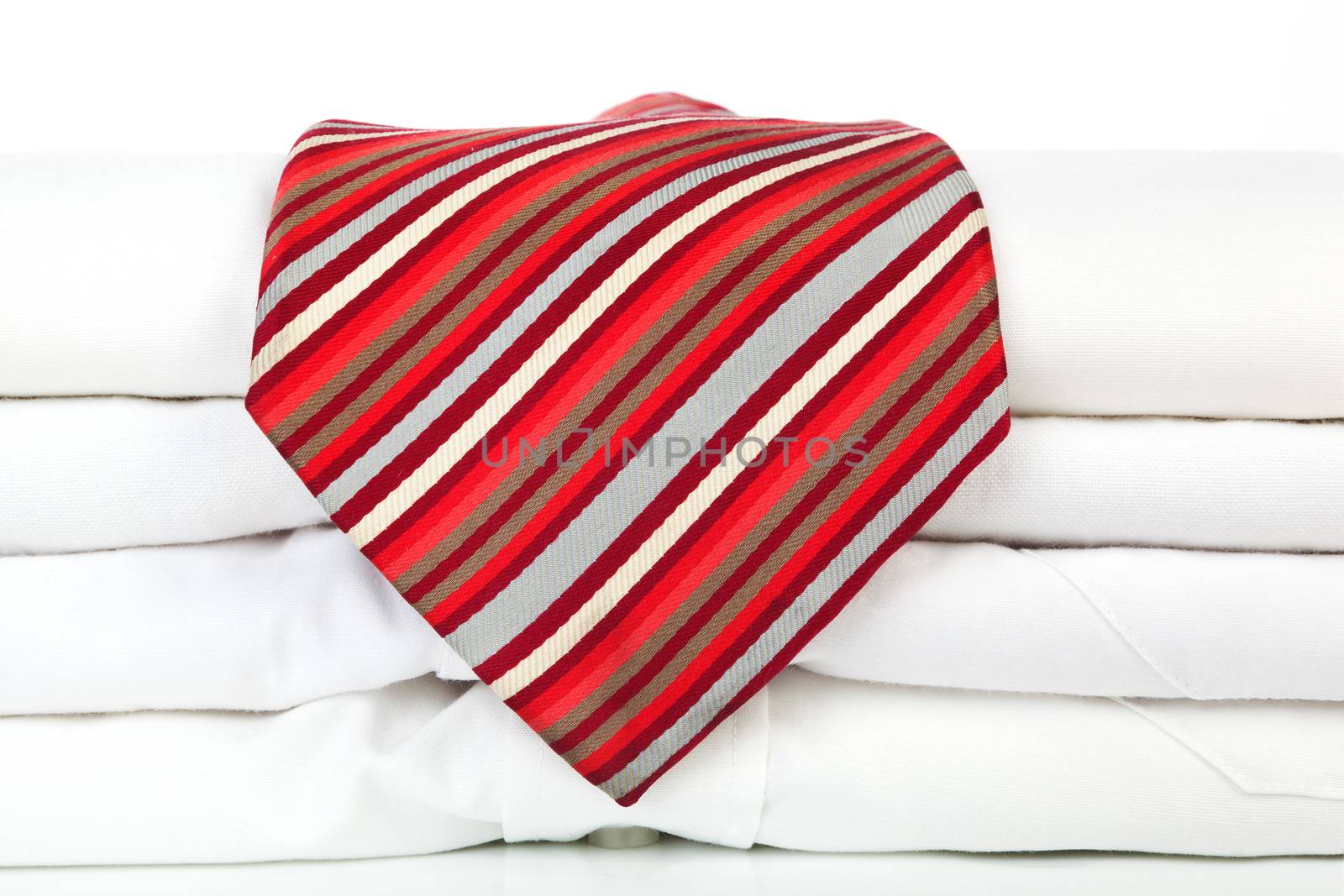 Pile of white business shirts with red striped tie on white background. Contemporary business concept.