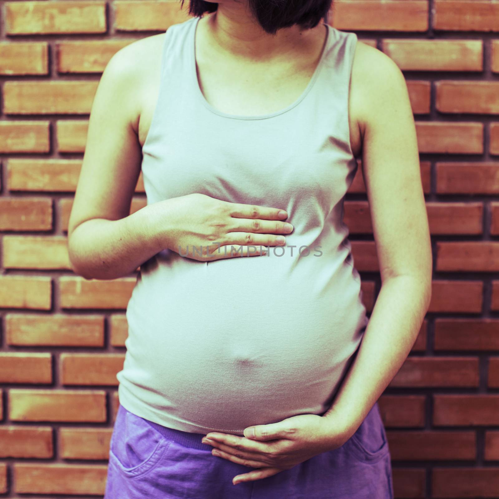 Image of pregnant woman touching her belly with hands on front o by 2nix