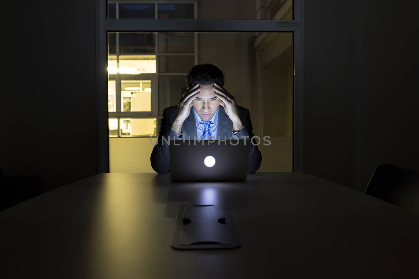 Businessman working late in his office on laptop, night light bu by LDProd