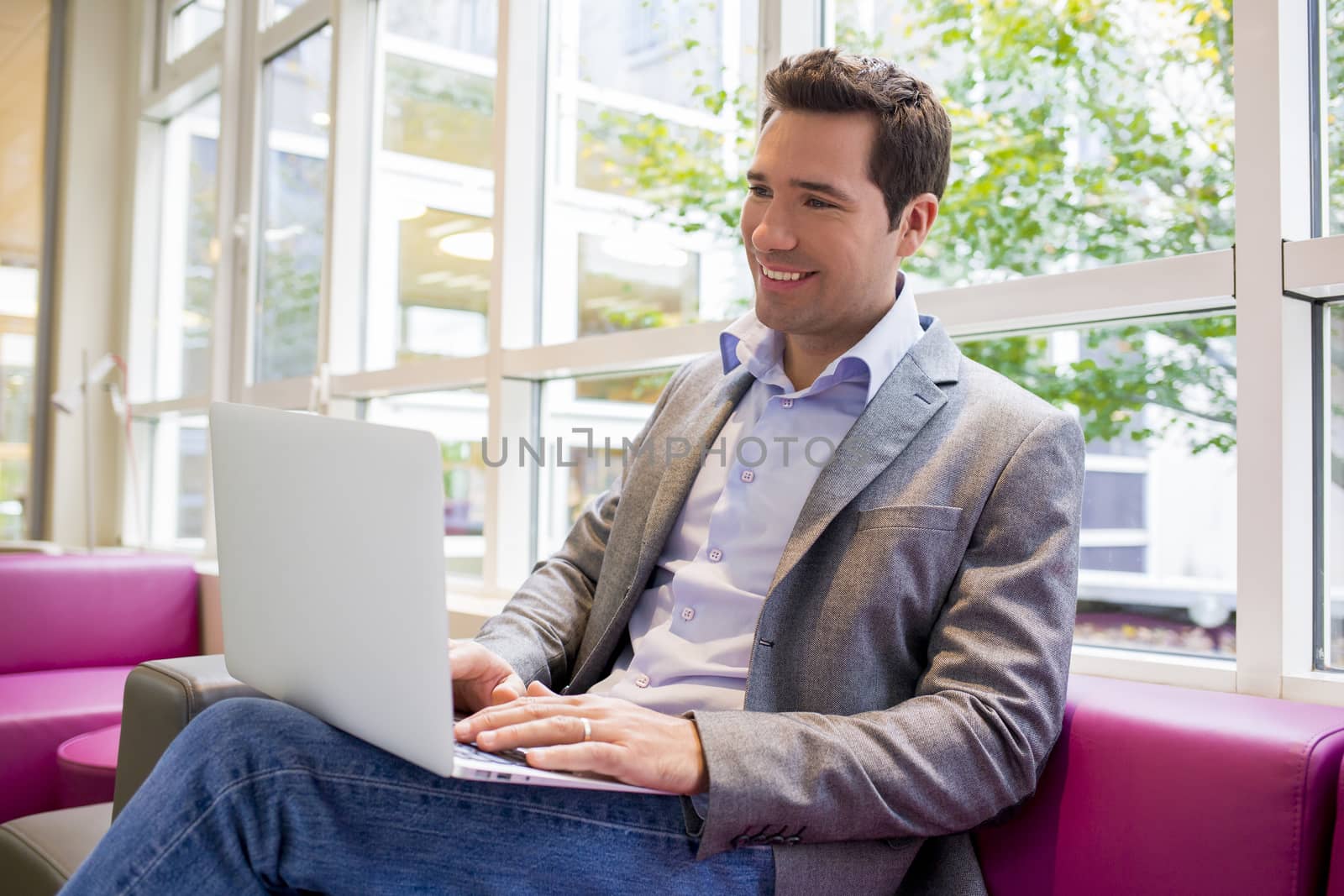 Happy smiling young Businessman  working with Laptop on sofa by LDProd