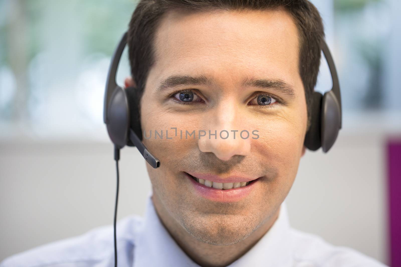 Businessman in the office on the phone with headset, looking cam by LDProd