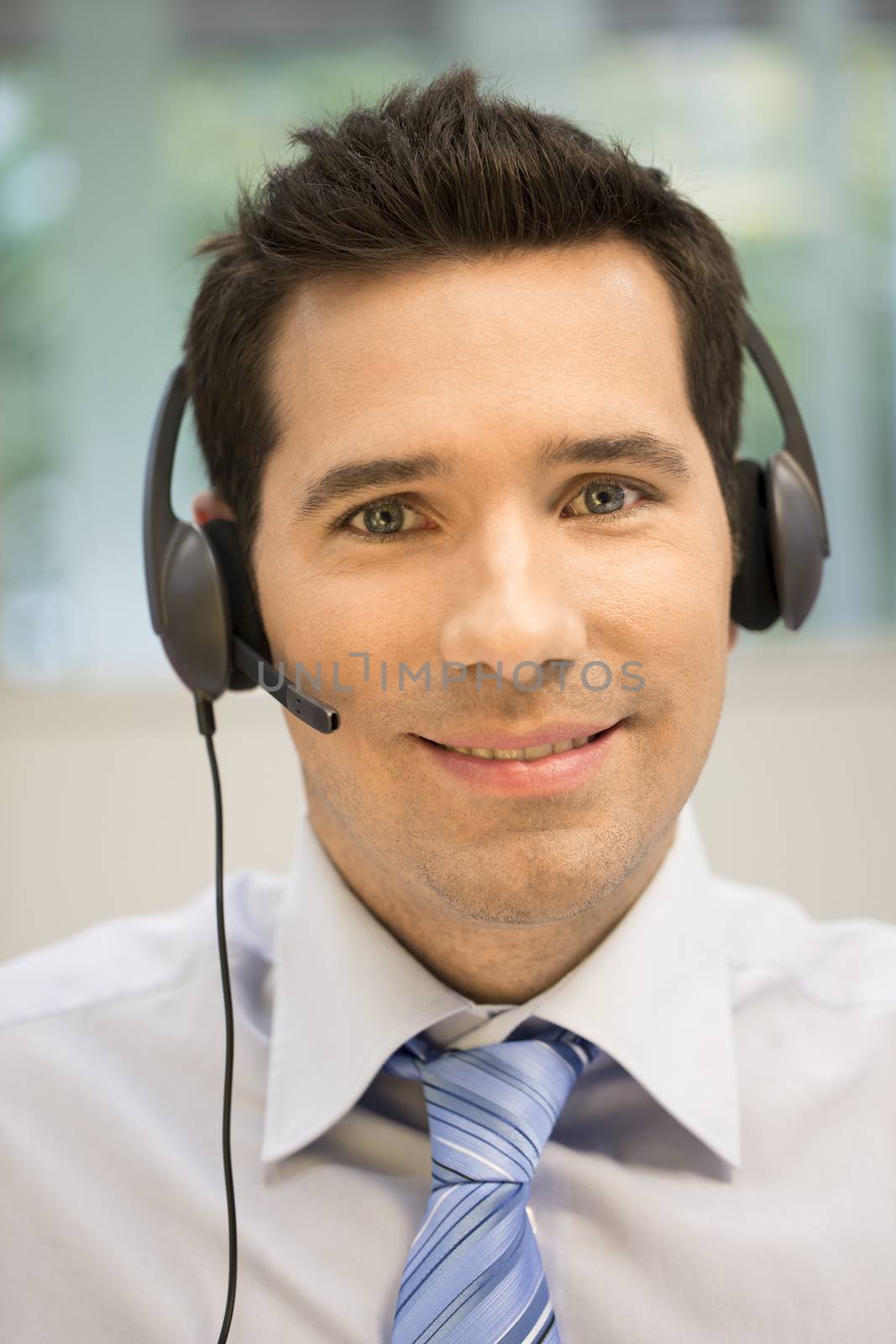 Businessman in the office on the phone with headset, looking cam by LDProd