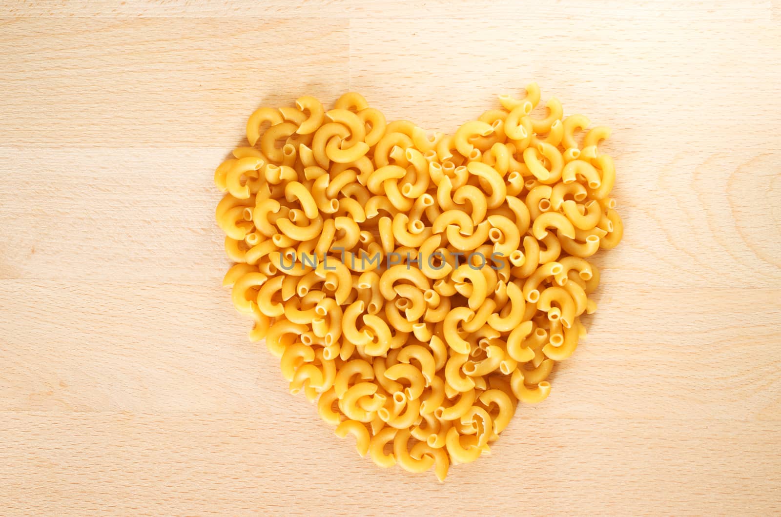 Macaroni forming a heart over a wooden cut board. Concept of healthy food. 