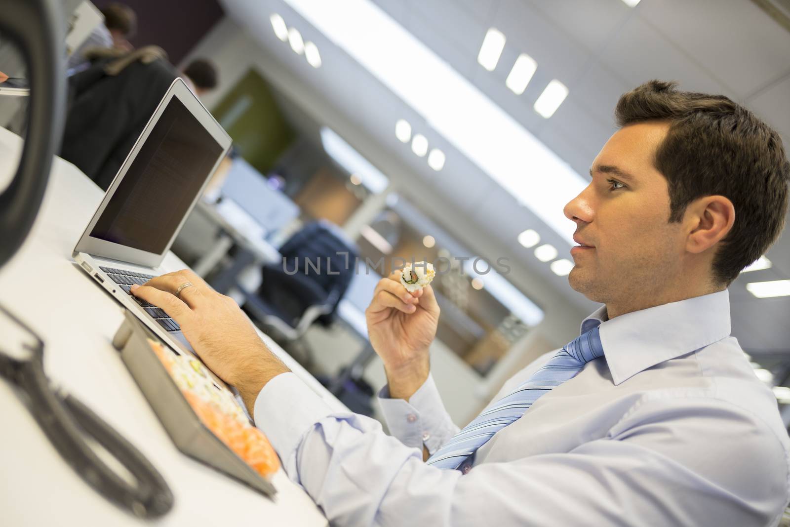 Businessman with laptop eating sushi on his desk by LDProd