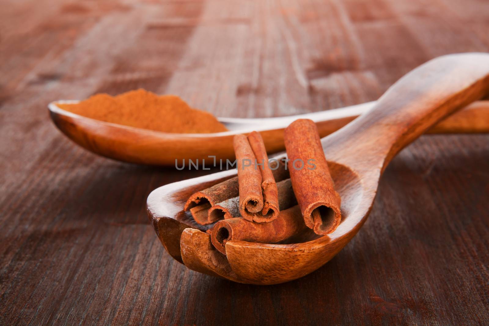 Cinnamon sticks on spoon and cinnamon powder on wooden spoon in background. Brown natural culinary spice concept.