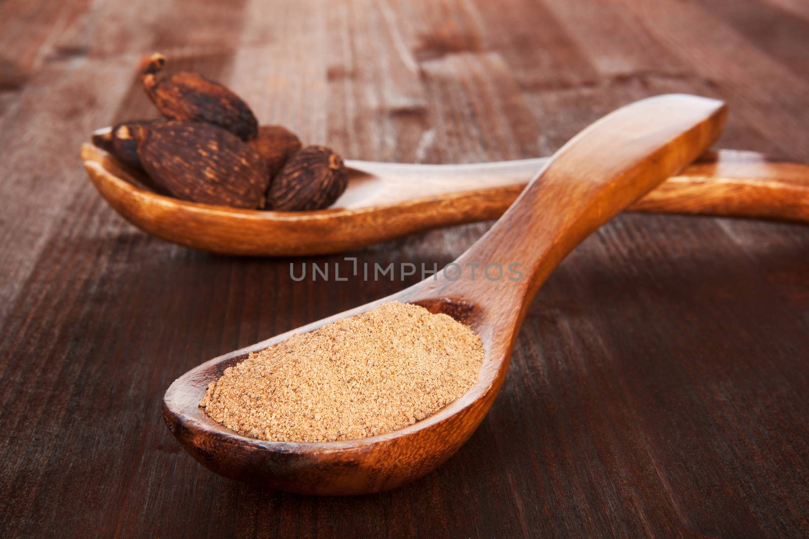 Grated nutmeg in wooden spoon and whole nutmegs on wooden spoon in background on dark wooden background. Culinary aromatic spice.