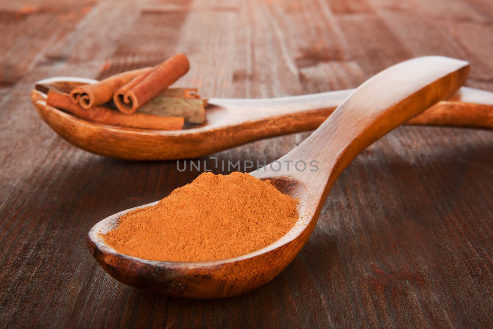 Cinnamon concept. Sticks and powder on wooden spoons on wooden background. Aromatic culinary spices.