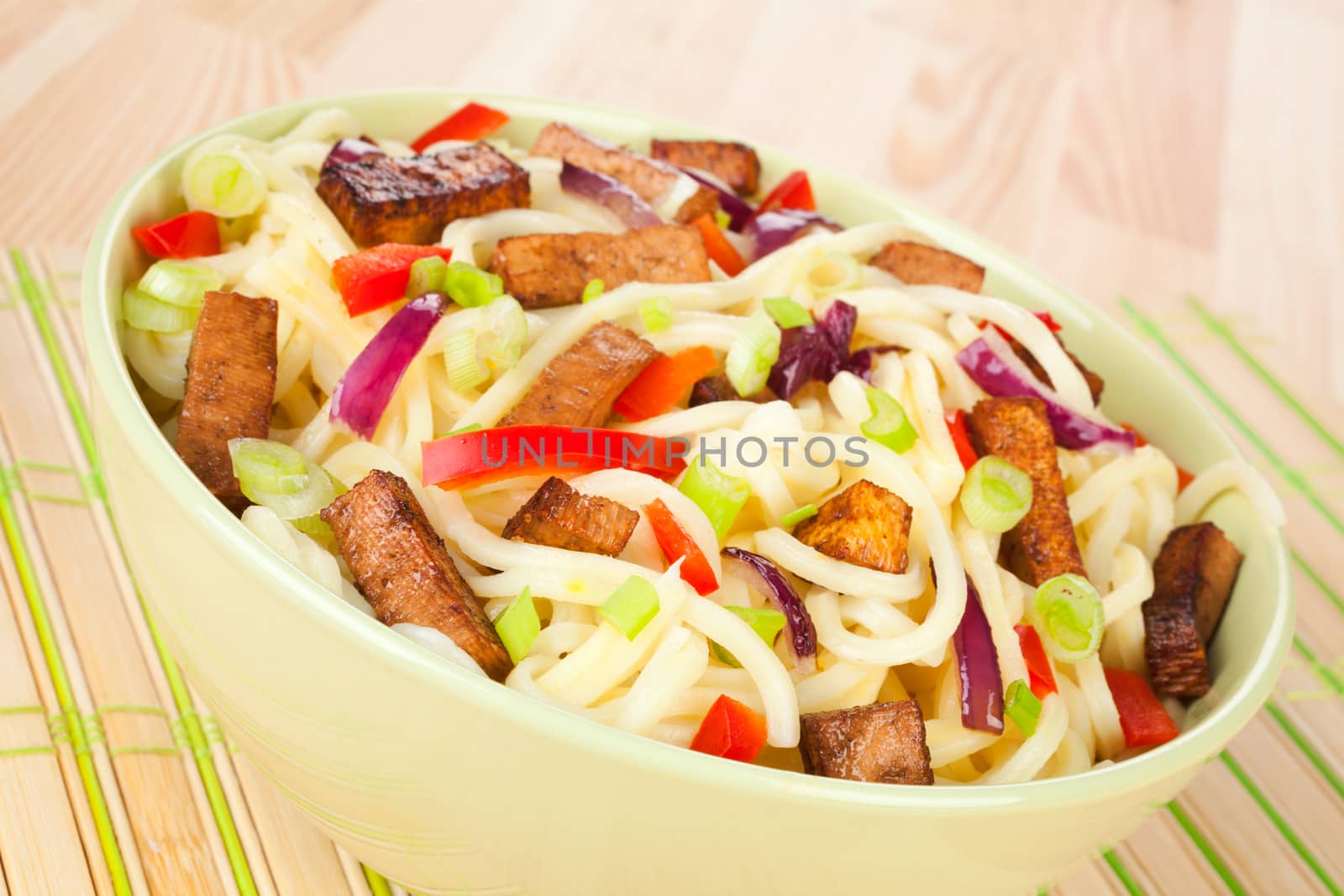 Traditional asian noodles with vegetable and tofu in green bowl on light wooden background. Asian culinary food.