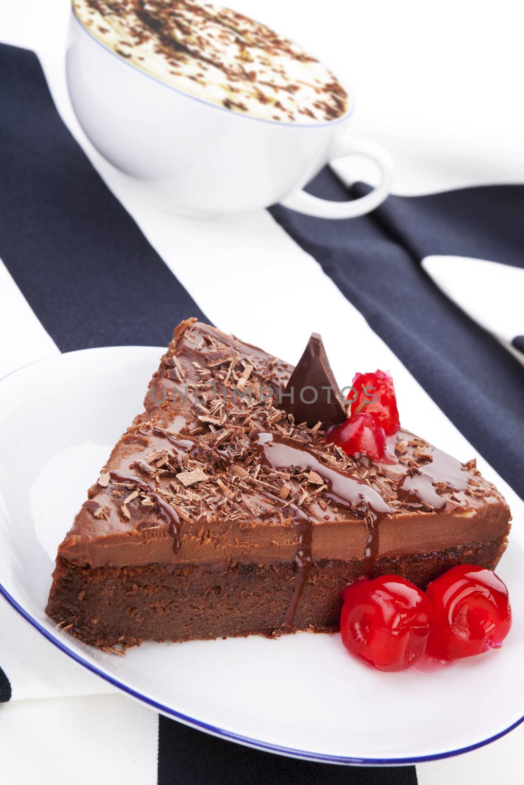 Delicious homemade chocolate cake with cappuccino in cup in background. Culinary sweet desert still life.