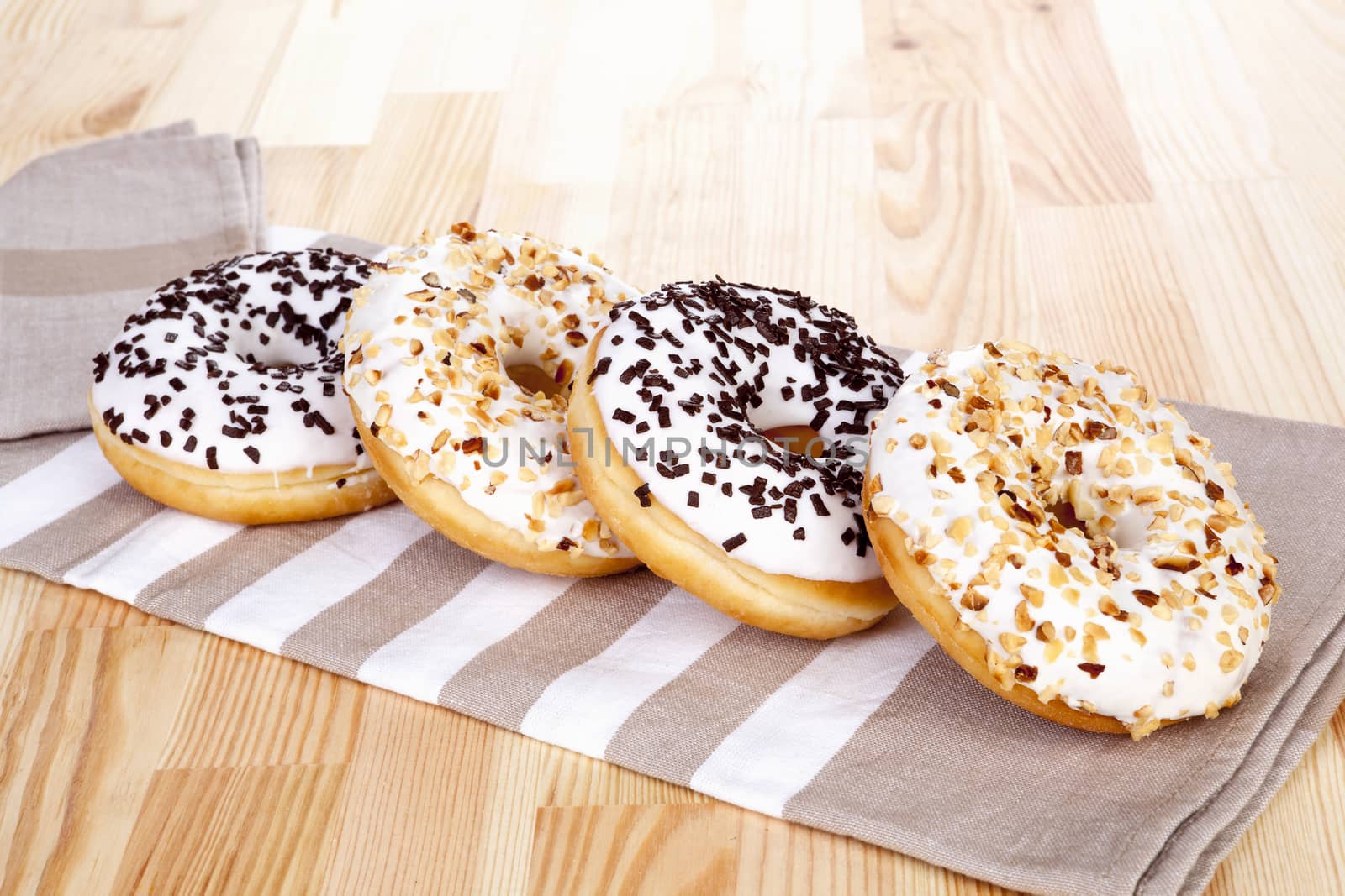 Chocolate and nuts donuts on kitchen cloth on light wooden background. Culinary sweet breakfast.