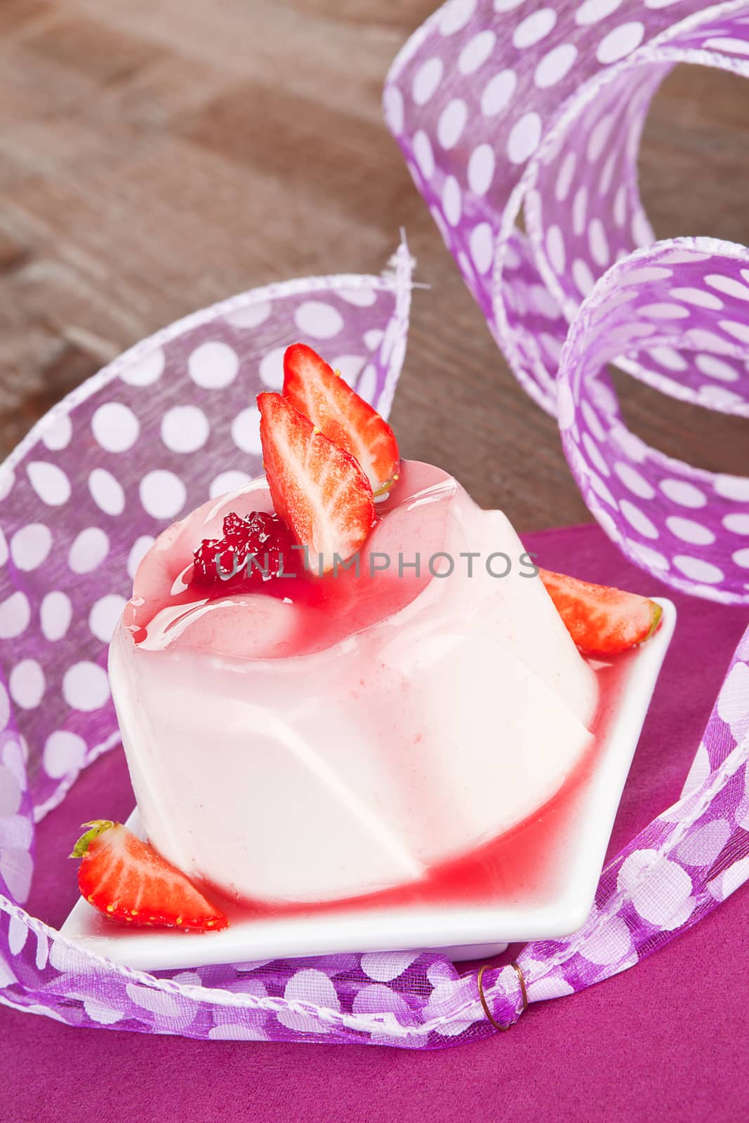 Delicious pudding with fresh strawberries and cream on purple and wooden background. Culinary sweets concept.