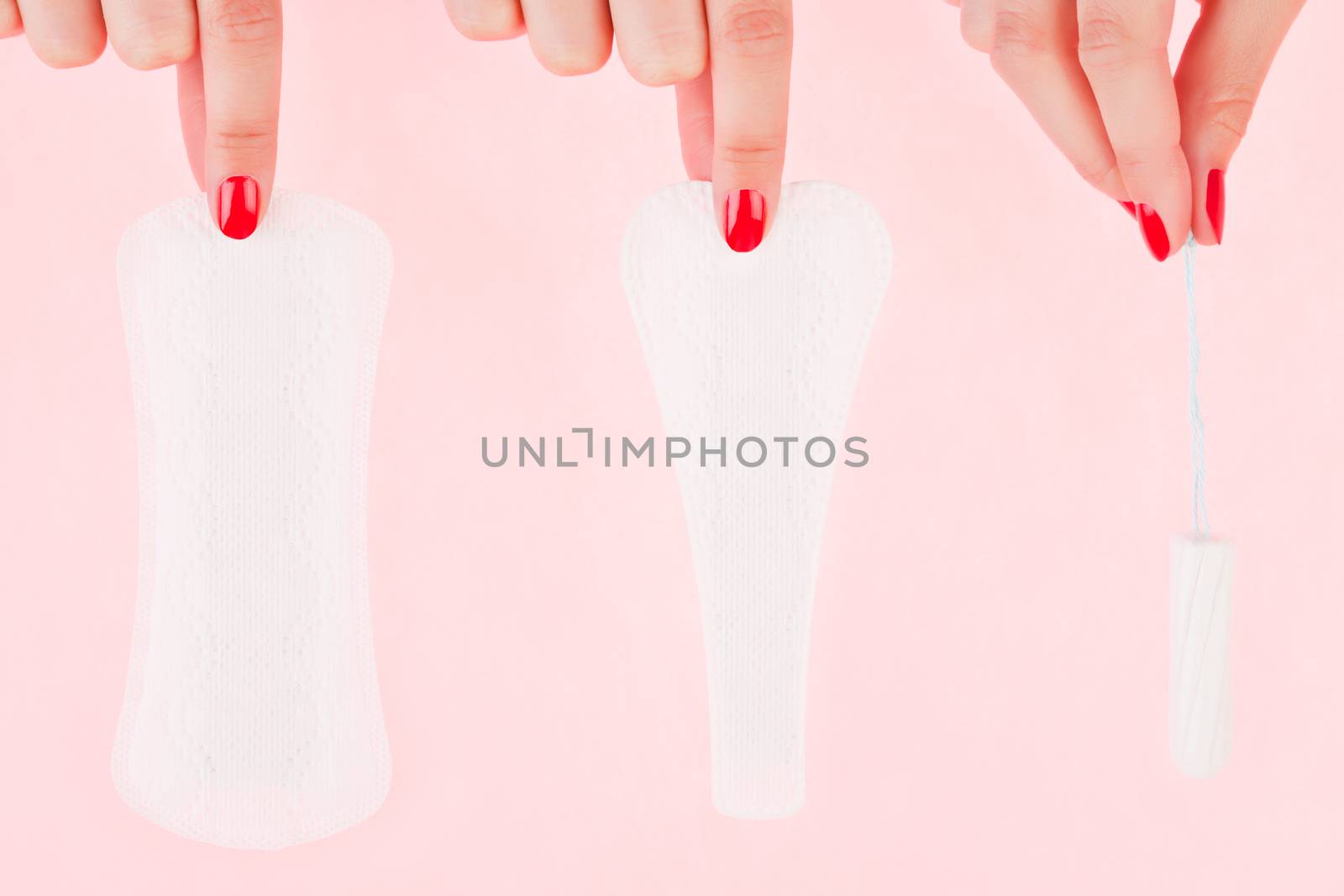 Female hand with red fingernails holding a clean pantyliner, g - string pantyliner and a tampon isolated over pink background. Feminine hygiene concept.