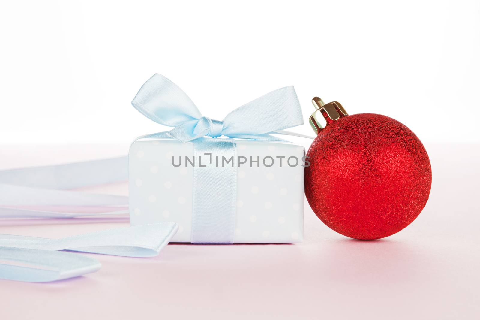 Luxurious gift and christmas ball with ribbon on light pink background. Festive holiday background, giving concept.