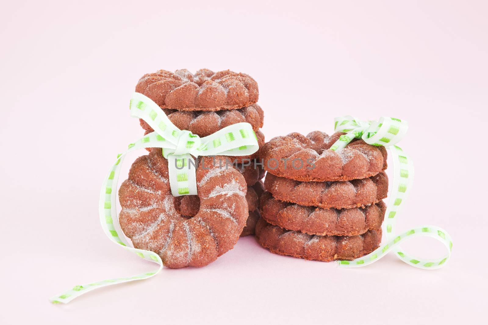 Sweets. Round chocolate cookies with green ribbon against pink background. Festive cookies.