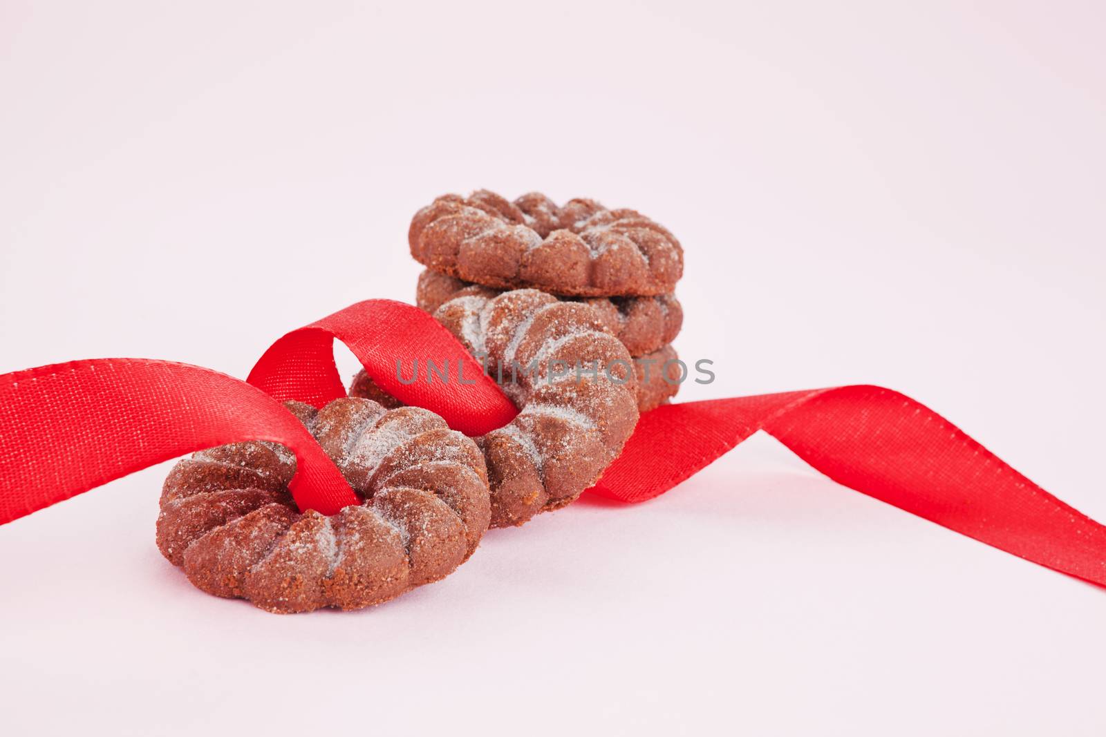 Chocolate cookies with red ribbon on pink background. Sweets.