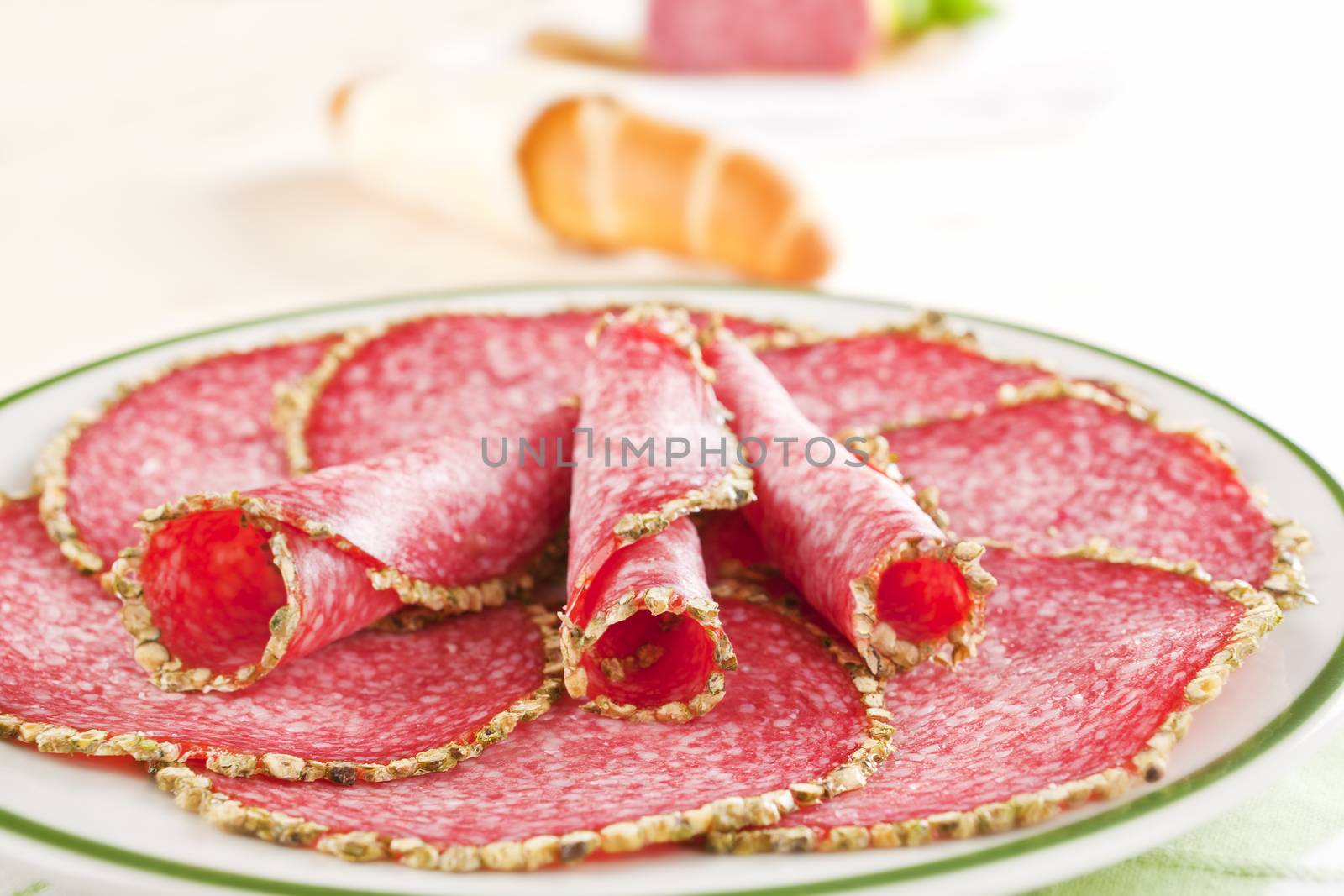 Delicious salami slices arranged on plate. Pastry in background. Culinary meat concept.