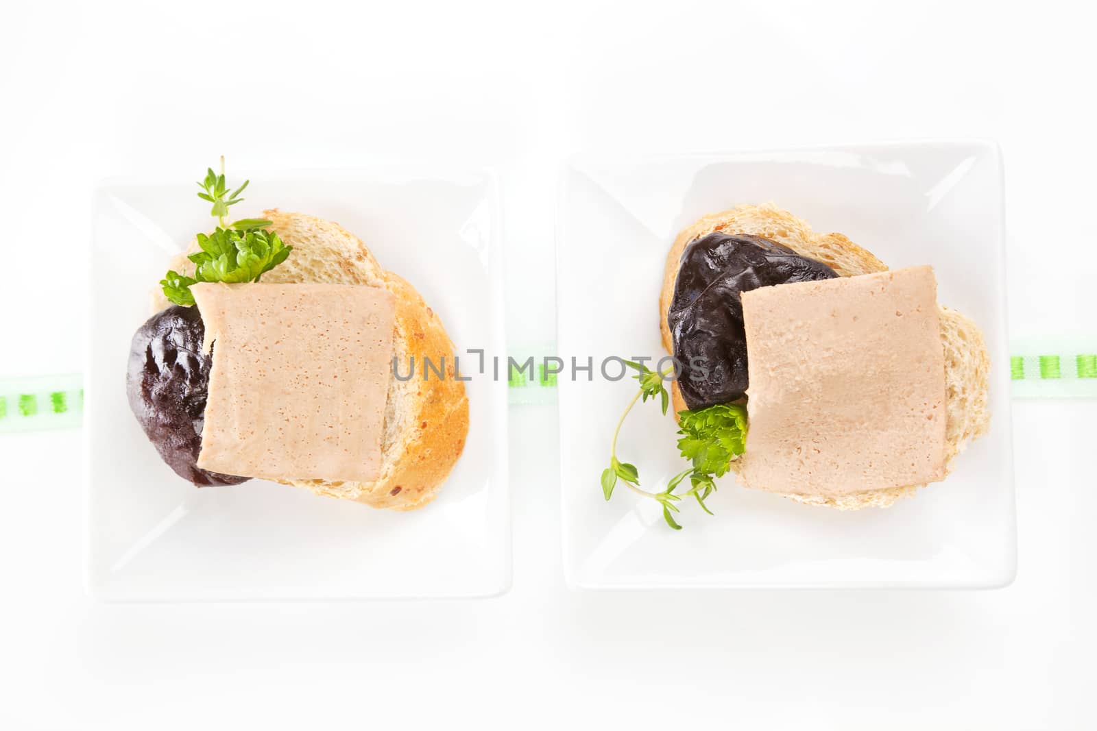 Two white bread pieces in white square bowls with delicious pate, dried plum and fresh herbs.