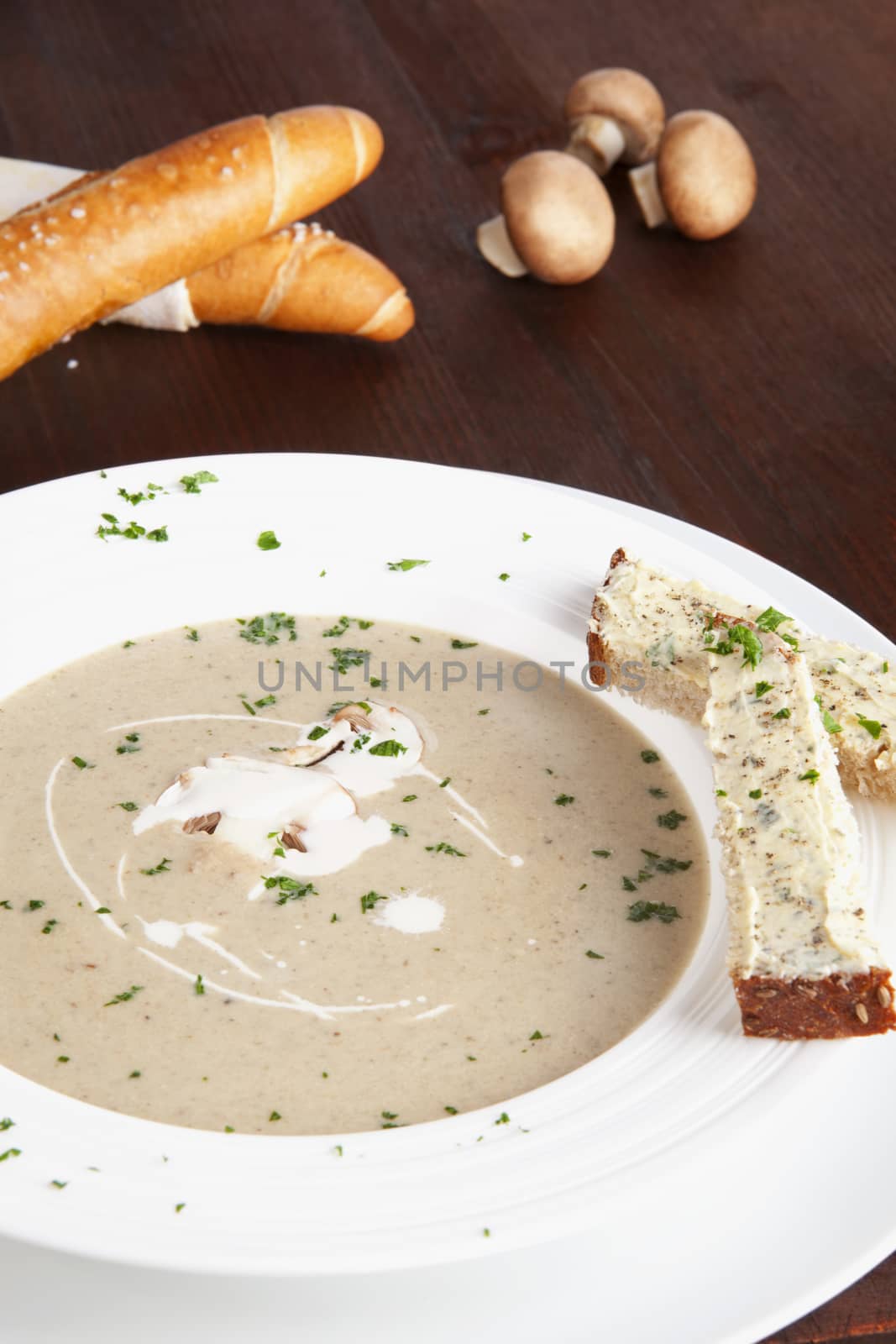 Delicious mushroom cream soup in white plate, pastry and fresh mushrooms in background. Culinary eating.
