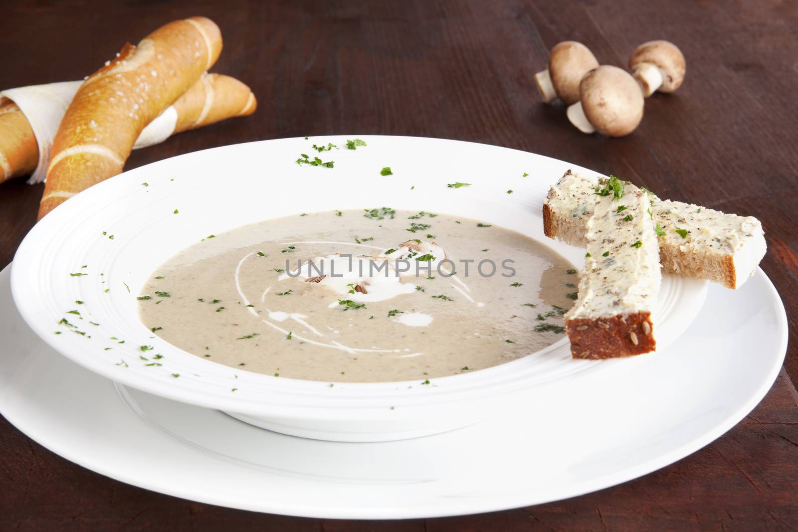 Champignon mushroom cream soup in white plate with pastry on dark wooden background. Culinary eating.