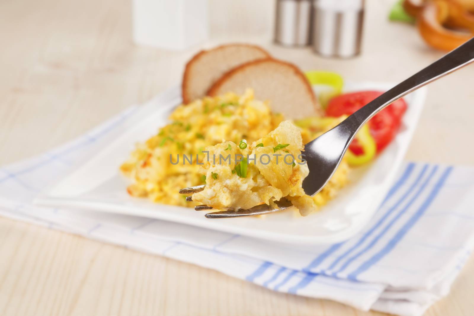 Culinary breakfast. Scrambled eggs on fork, pastry, salt and pepper shaker in background. Breakfast concept.