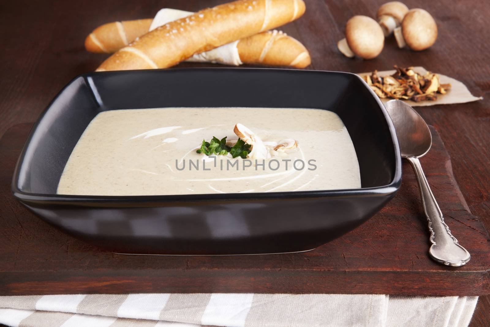 Luxurious champignon cream soup in black bowl. Mushrooms and pastry in background. Culinary eating concept.