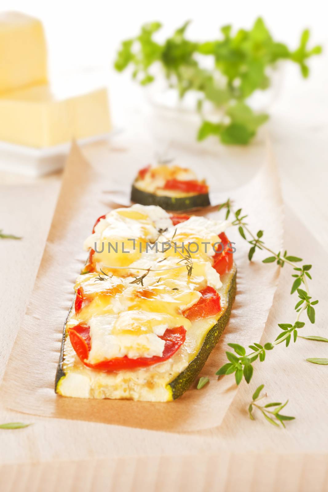 Baked zucchini slices with fresh tomatoes, cheese and herbs. Cheese and fresh herbs in background. Culinary healthy food.