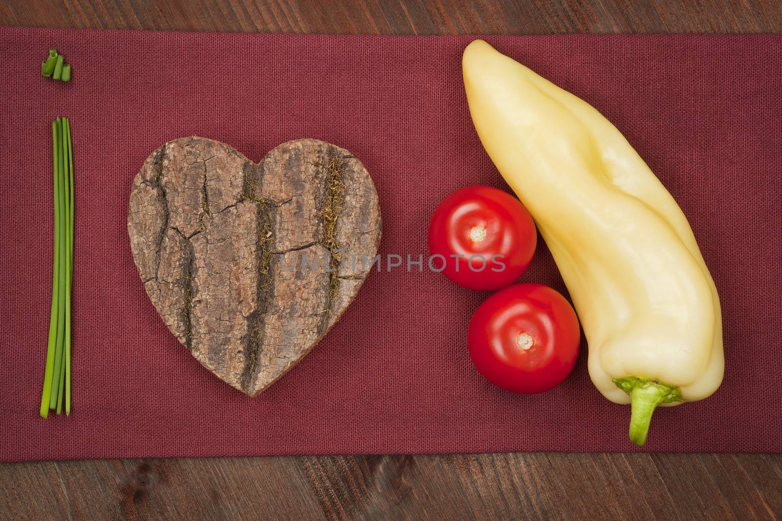 I love vegetable made of chive, wooden heart, tomatoes and green pepper on burgundy cloth. Agriculture background.