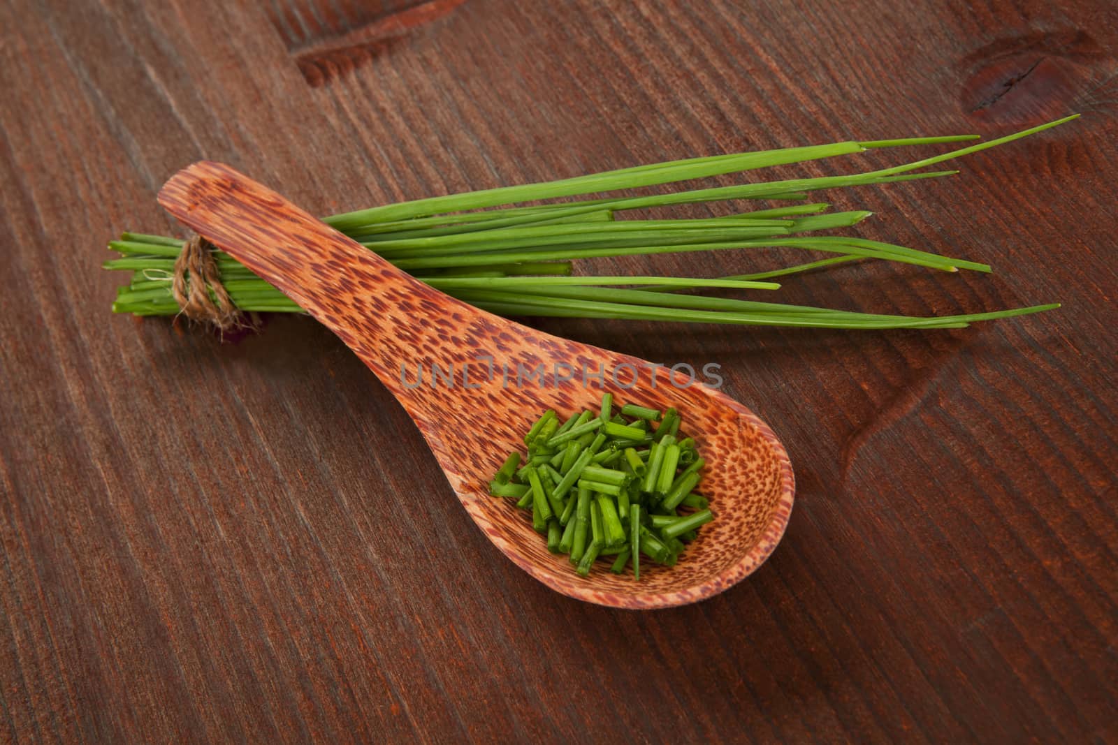 Fresh chopped chive on wooden spoon and chive bundle on dark wooden background. Aromatic culinary herbs.