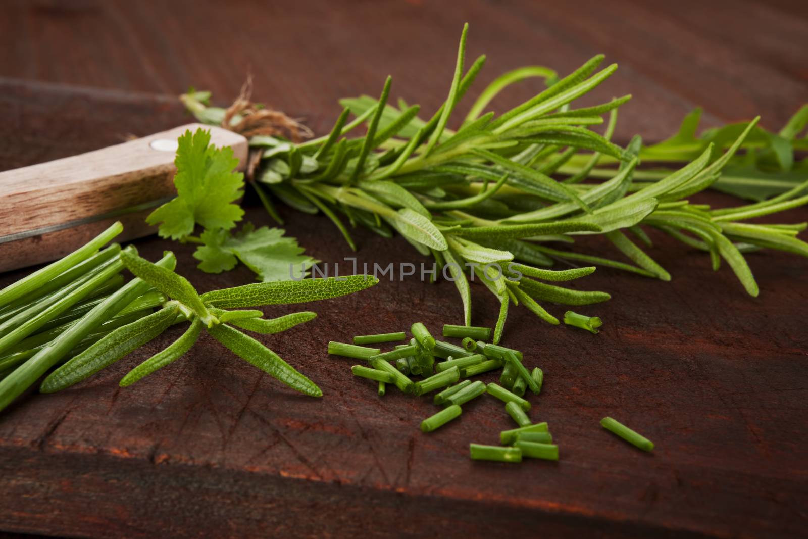 Fresh herb mixture on dark wooden cutting board. Chive, rosemary, coriander and arugula, aromatic culinary herbs.