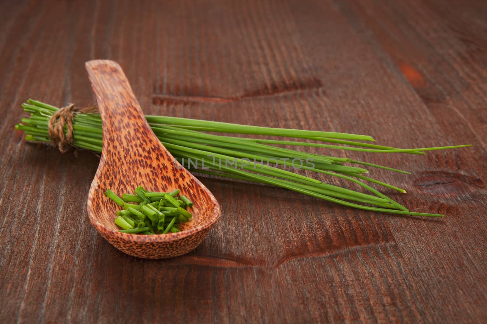 Fresh organic chopped chive on wooden spoon and chive bunch on dark wooden background. Aromatic culinary herbs.