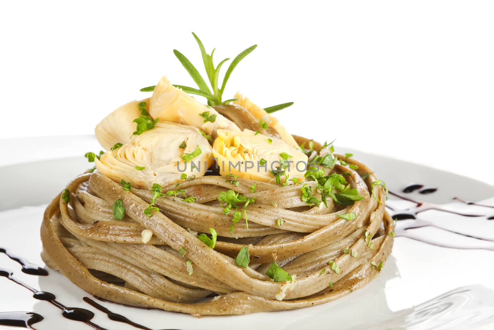 Homemade tagliatelle pasta with artichoke and fresh herbs on white plate. Luxury dining.