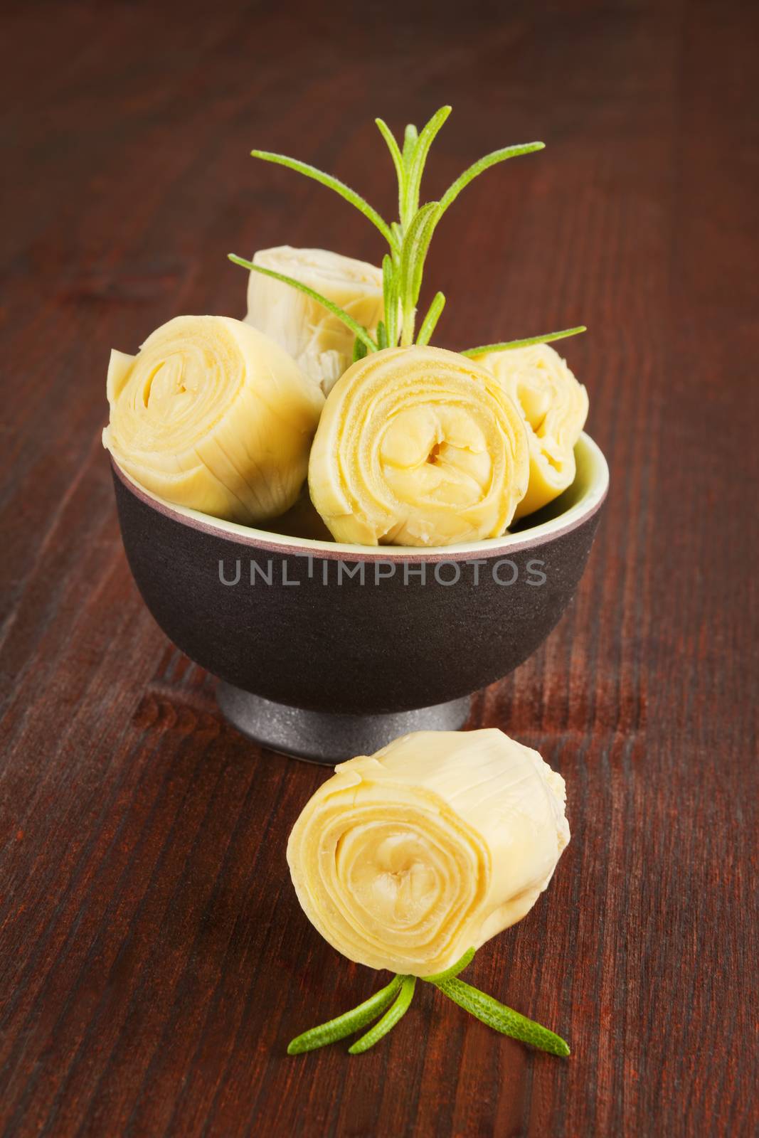 Artichoke in black bowl with fresh rosemary on dark wooden background. Culinary eating.