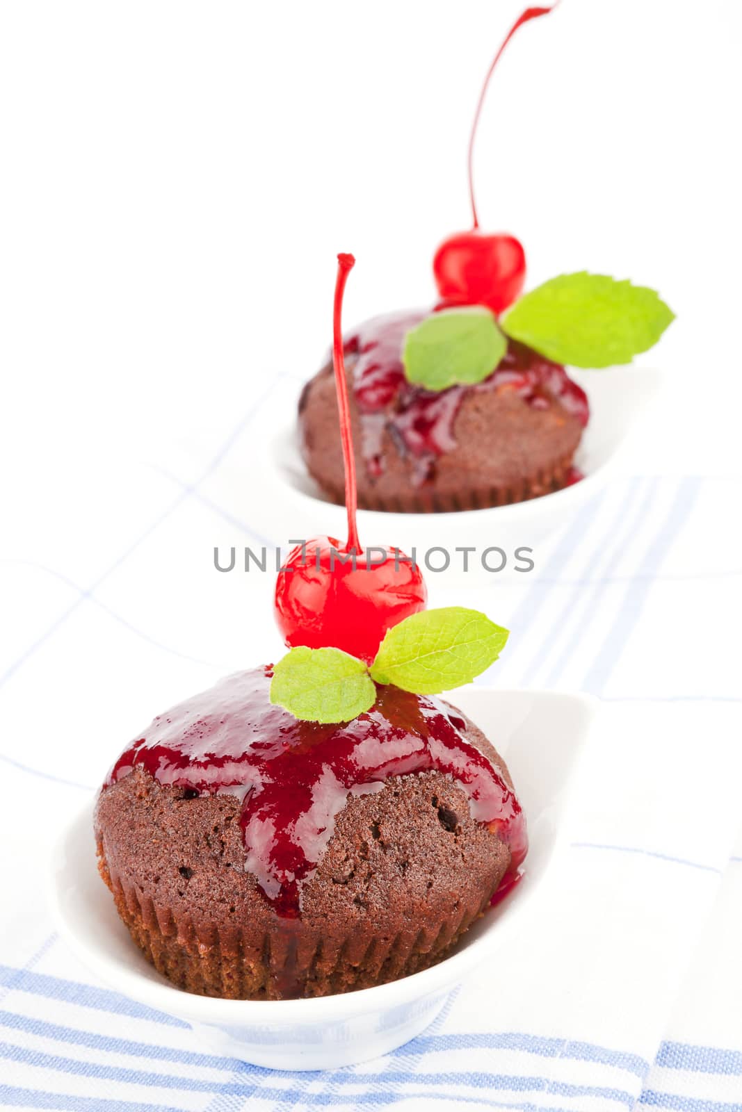 Delicious chocolate muffins decorated with jam, cherry and fresh mint leaf on kitchen cloth. Sweet culinary food.