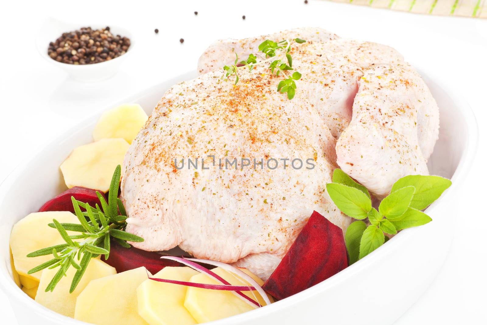 Raw chicken with fresh vegetable and herbs in baking dish prepared for baking.