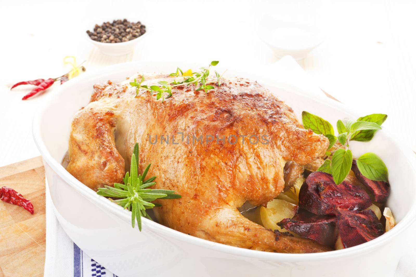Delicious golden grilled whole chicken with fresh herbs in baking dish.