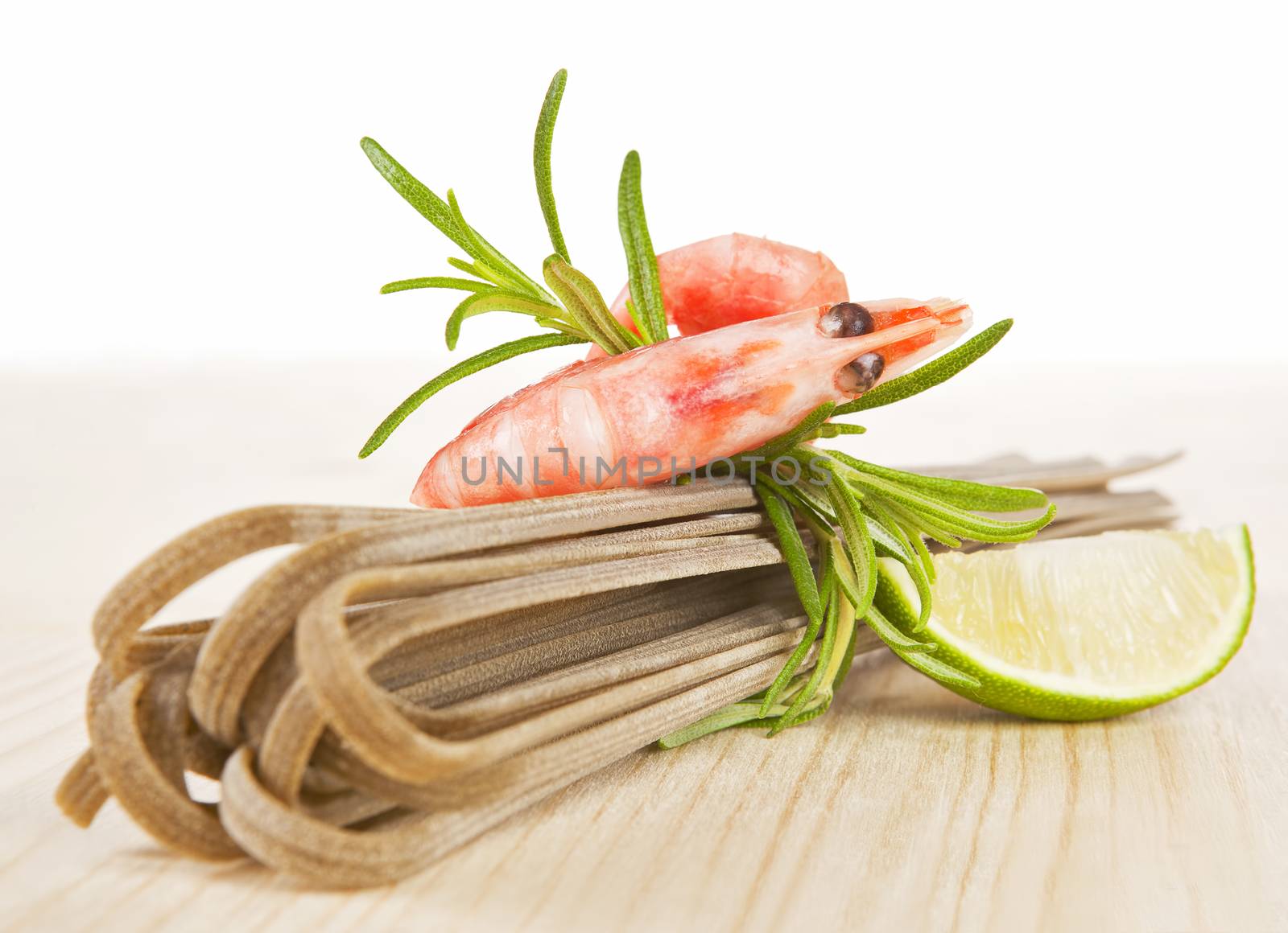 Whole grain pasta with shrimp, fresh rosemary and lime piece on wooden table.