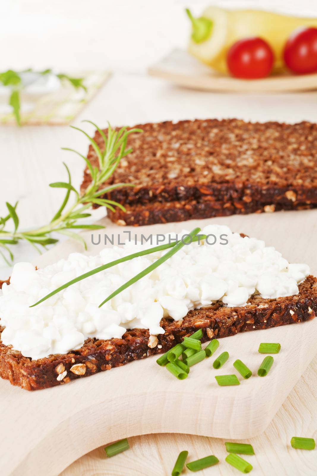 Luxurious black bread slices with cottage cheese with fresh herbs and vegetables on wooden cutting board. Healthy eating. 
