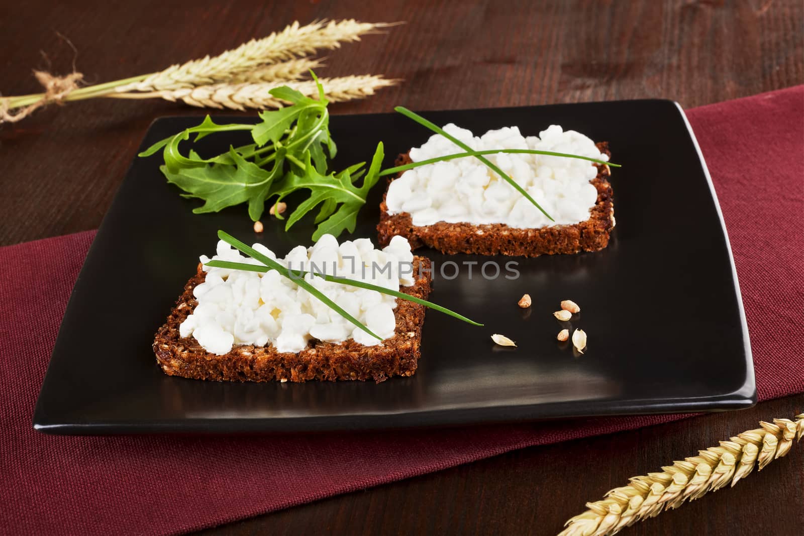 Black bread slices on black plate with cottage cheese and fresh herbs. Healthy eating background.