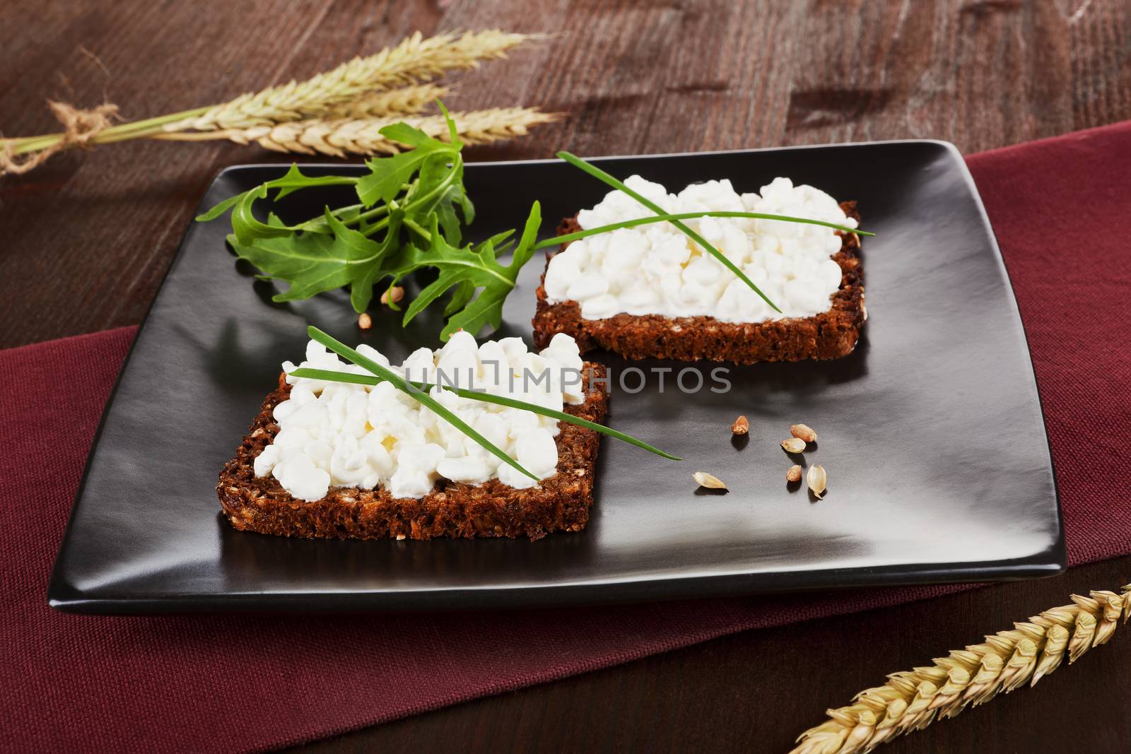 Two slices on black whole wheat bread with cottage cheese and fresh chive and arugula on black plate. Healhty eating background.