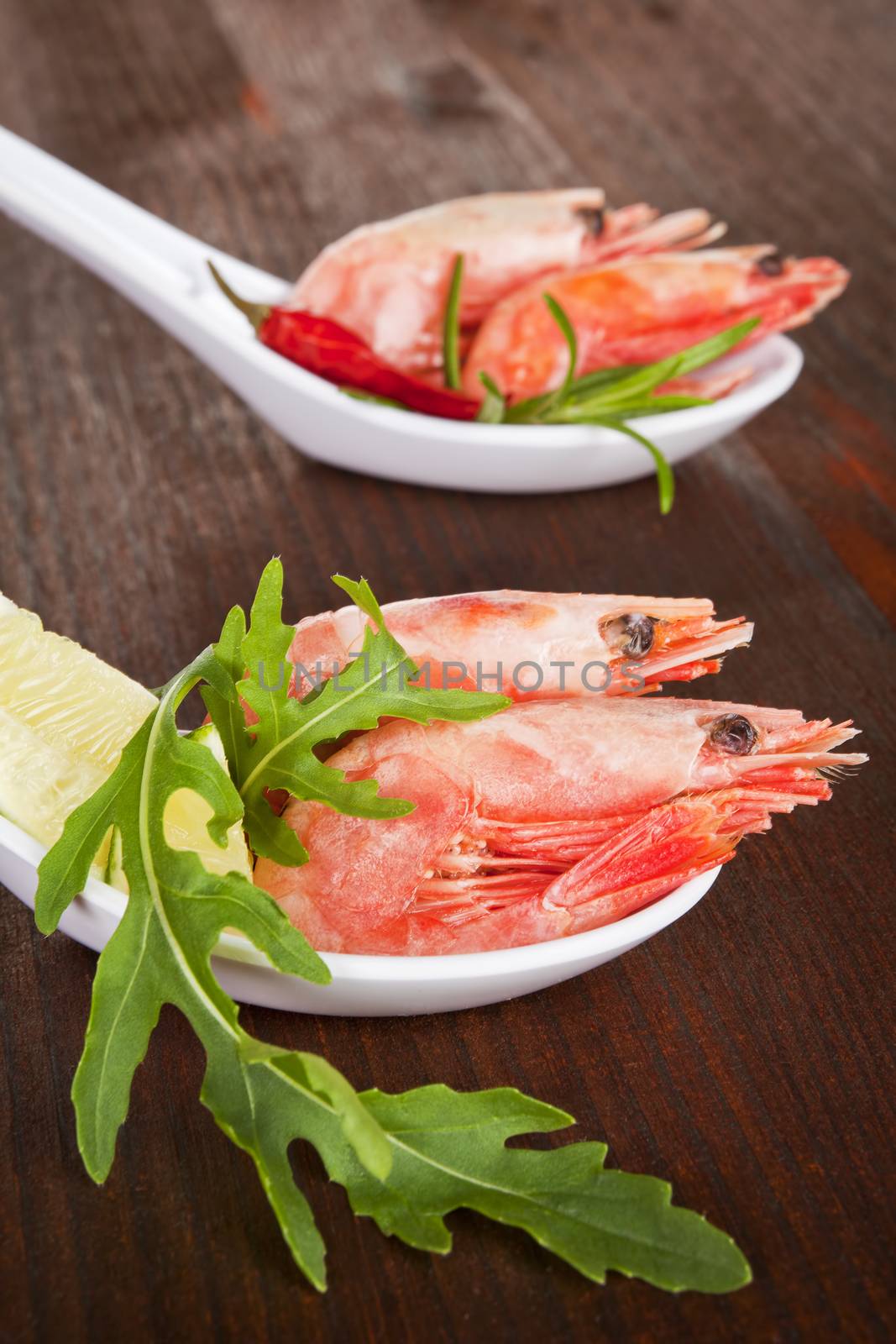 Luxurious seafood. Shrimps on white spoon with herbs close up.