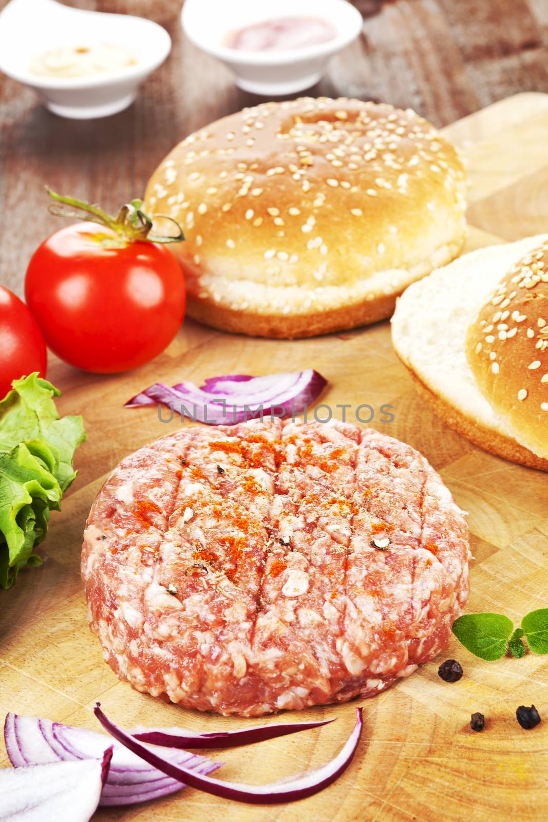Minced meet prepared for hamburger with bun, tomato, lettuce, mustard and ketchup in background. 