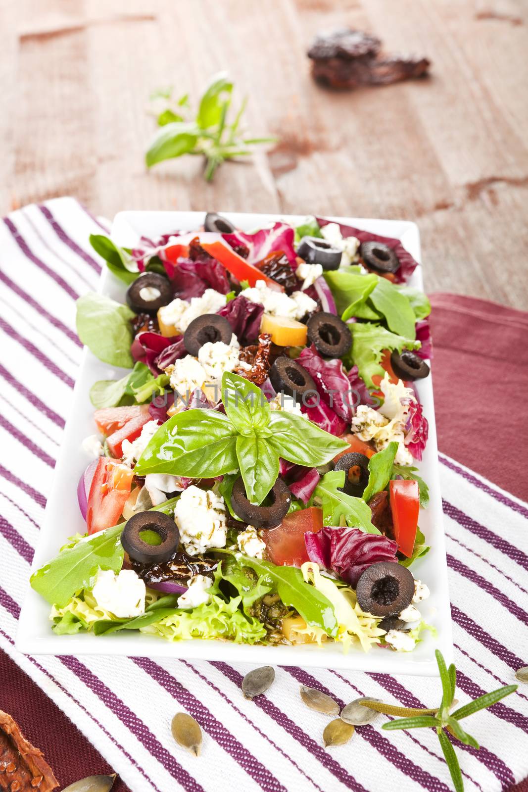 Tasty summer salad with fresh ingredients and herbs on kitchen towel on dark wooden table. 