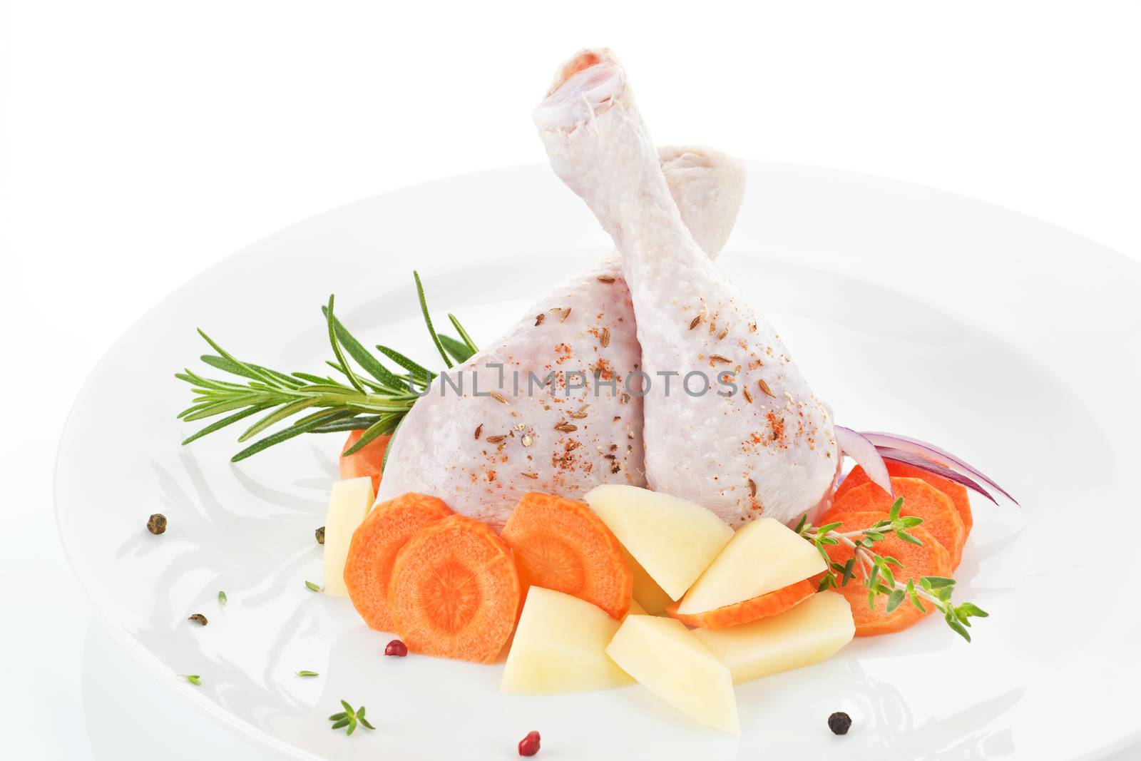 Two chicken legs with fresh vegetables and herbs on white plate. 