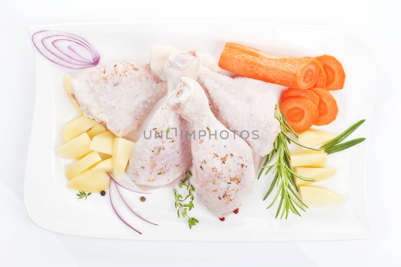 Raw chicken legs with potatoes, onions and carrots on white tray isolated on white background. 