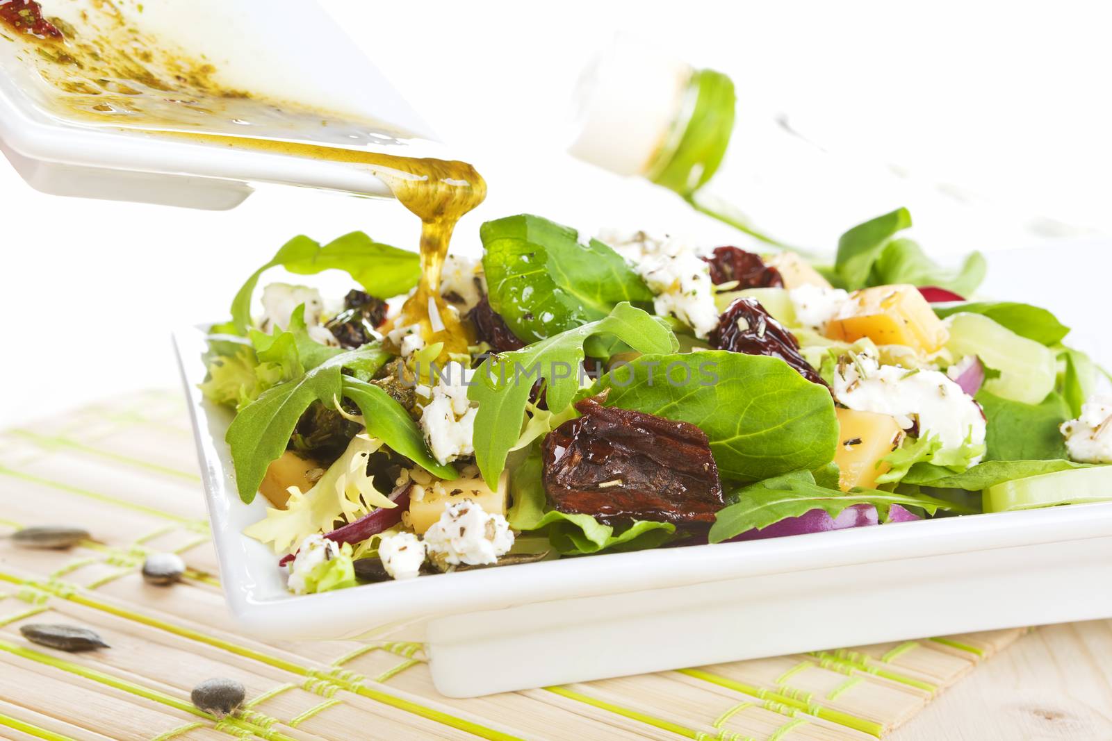 Pouring olive oil dressing on fresh goat cheese salad in white plate. 