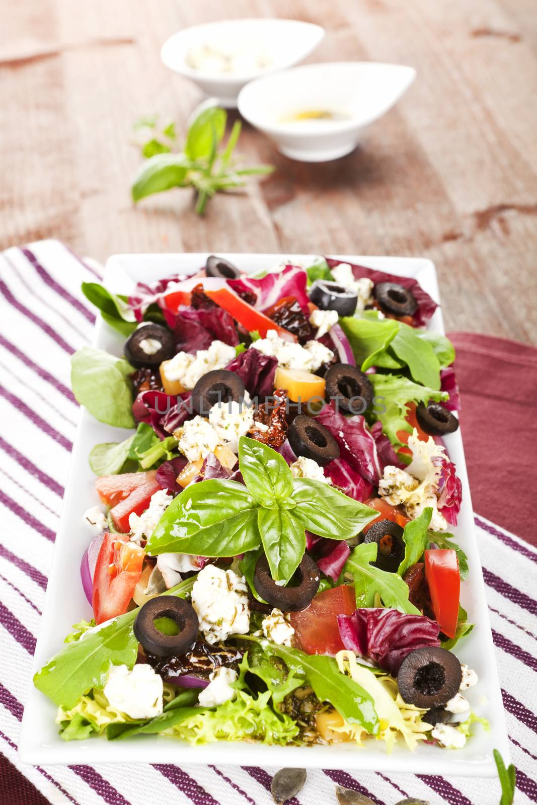 Colorful fresh salad with feta, goat cheese, olives, tomatoes and arugula.