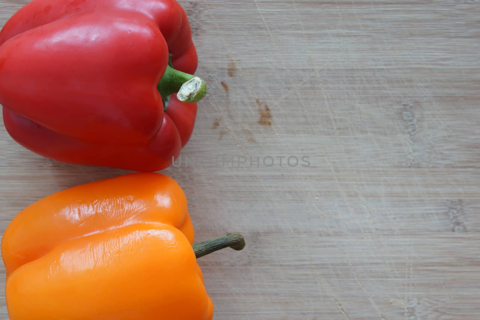 A red and orange pepper on a wooden cutting board