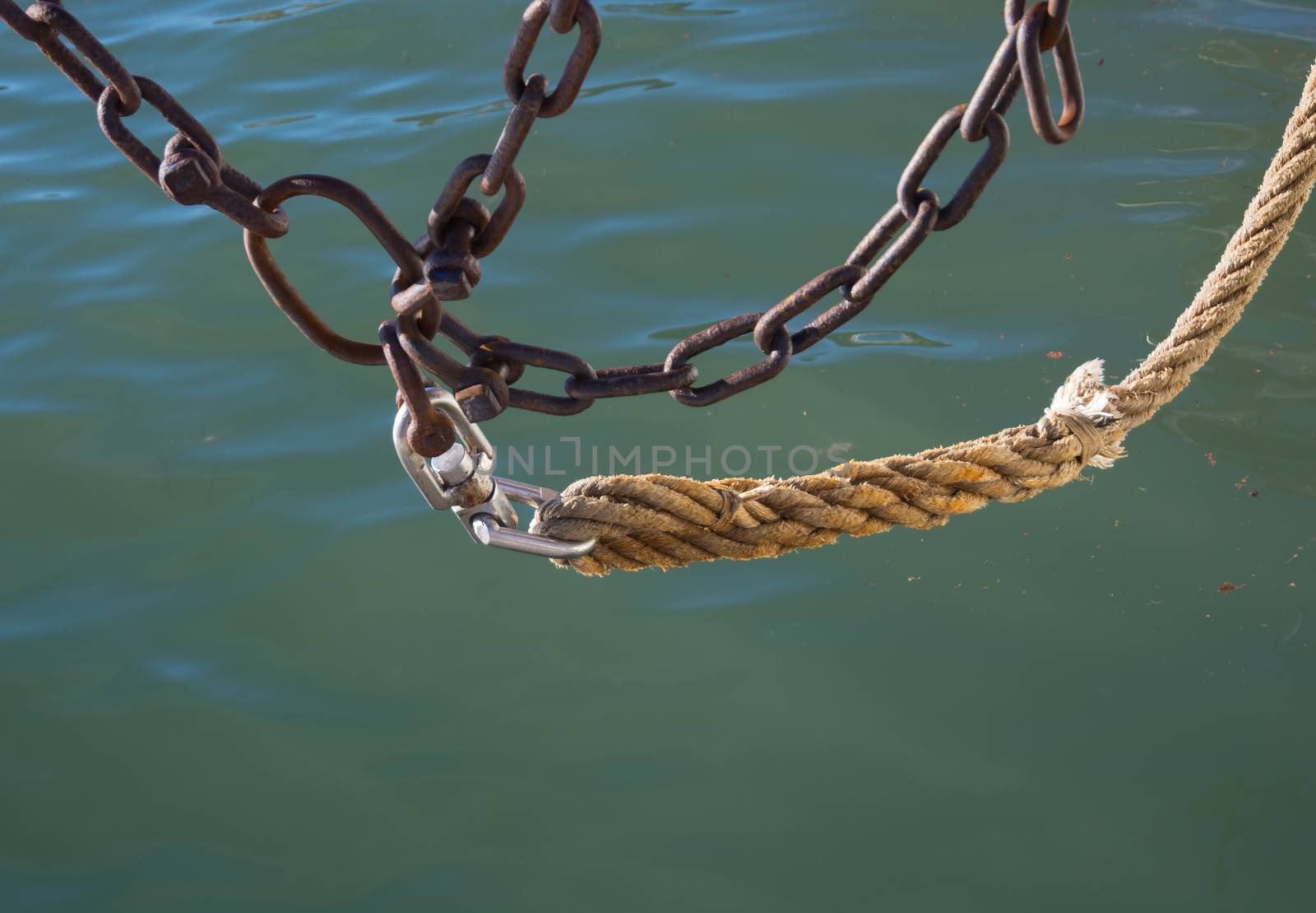 Chains and rope above green mediterranean ocean water.