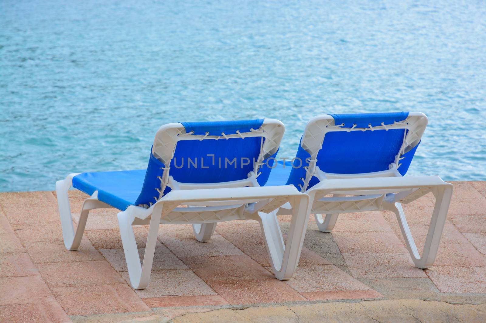 Two empty blue lounge chairs by the ocean.